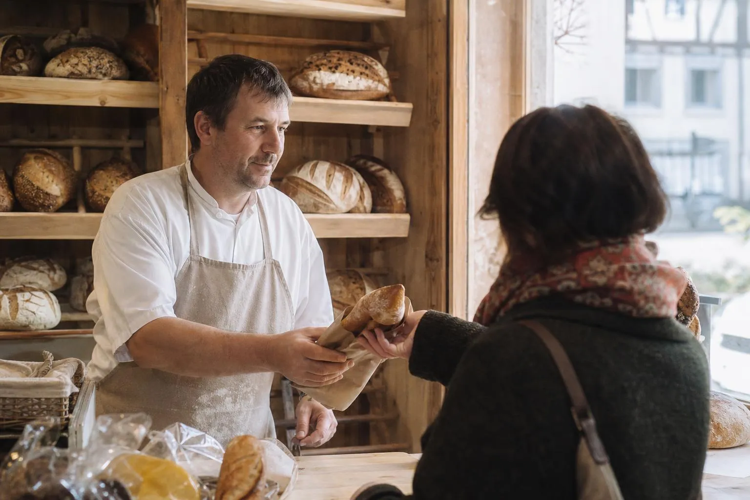 Un boulanger tend une baguette à une cliente par-dessus le comptoir